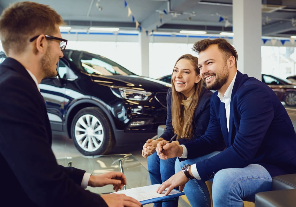Introverted car salesperson attentively listening to smiling couple during a sales meeting at a dealership